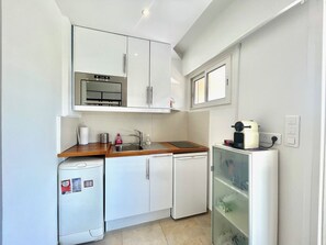 Une cuisine compacte avec des meubles blancs, un évier en acier inoxydable, un petit réfrigérateur et une machine à café.