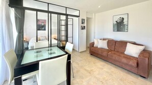 Una sala de estar moderna con una mesa de comedor de vidrio, un sofá marrón y un separador de vidrio.