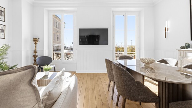 Ein modernes Wohnzimmer mit Holzboden, einer Couch, einem Esstisch mit Stühlen und einem an der Wand befestigten Fernseher.