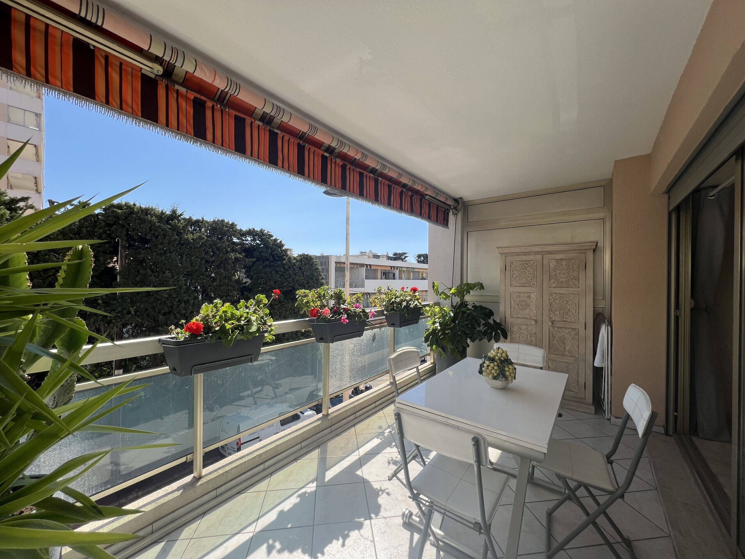 A balcony with a white table and chairs, potted plants, and a view of the city.