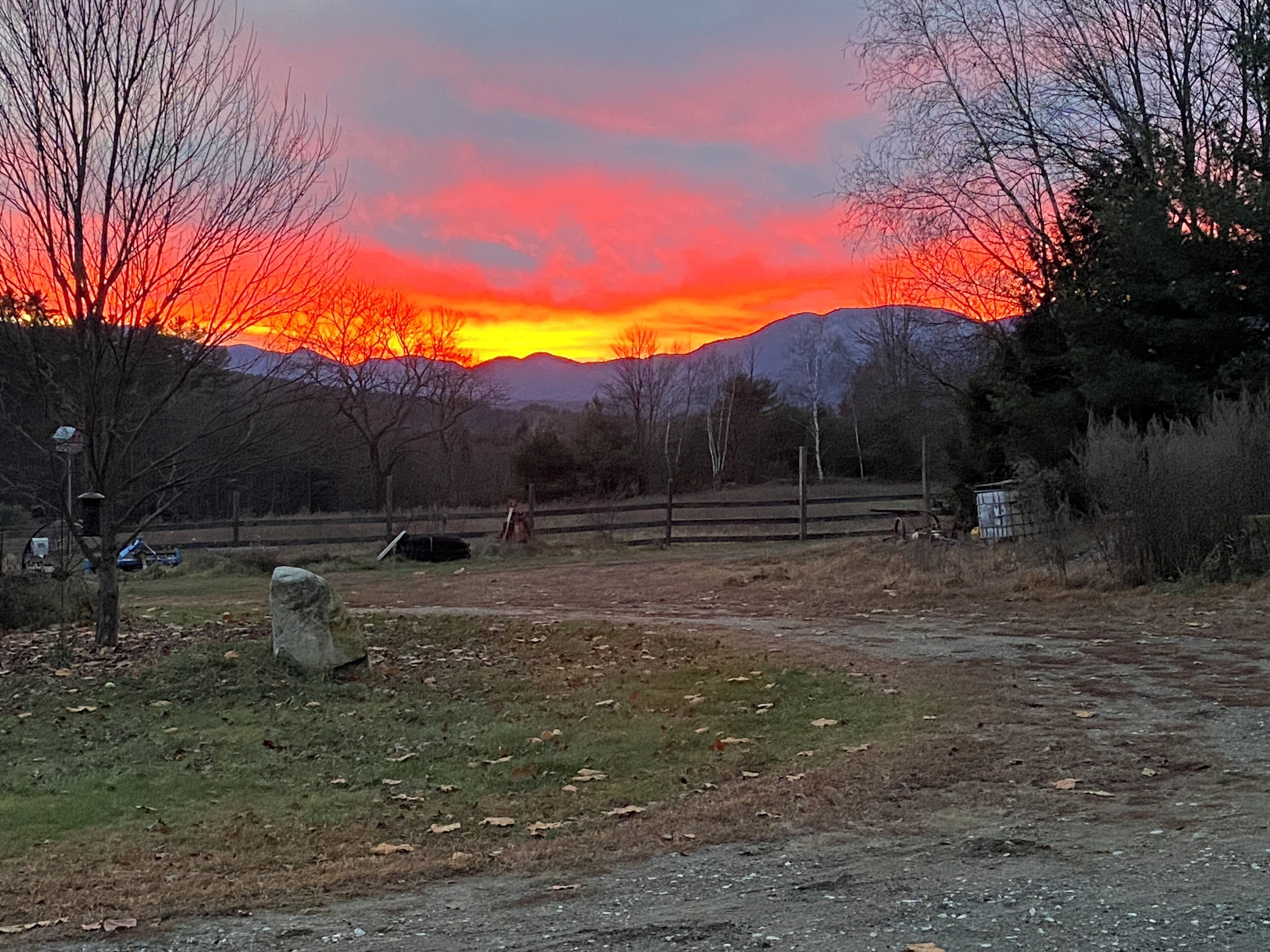 Paisaje rural con un atardecer, campos abiertos y una cadena montañosa al fondo.