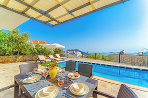 An outdoor dining area with a pool, chairs, and umbrellas. - Villa Meltem Luxury Villa with Private Pool & Panoramic Sea Views – Kalkan (Antalya)