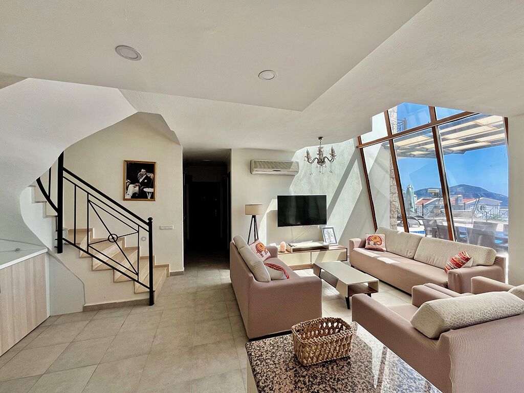 A spacious living area with a staircase, a flat-screen TV, and a large window offering a city view.