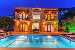 A two-story house with a swimming pool, stone facade, and outdoor seating area. - Villa Meltem Luxury Villa with Private Pool & Panoramic Sea Views – Kalkan (Antalya)