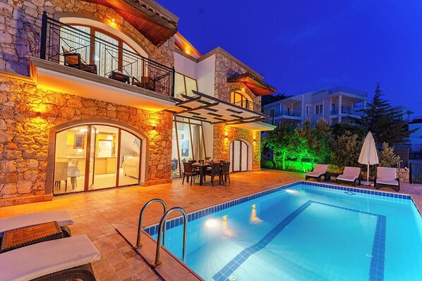 A modern villa with a swimming pool, stone facade, and outdoor seating area. - Villa Meltem Luxury Villa with Private Pool & Panoramic Sea Views – Kalkan (Antalya)