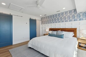 Een slaapkamer met een groot bed, een plafondventilator en een behang met patroon.