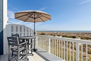 Um terraço com mesa, cadeiras, um guarda-sol e vista para a praia e o oceano.