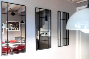 Trois miroirs sur un mur, un coin repas avec des chaises rouges et un escalier.
