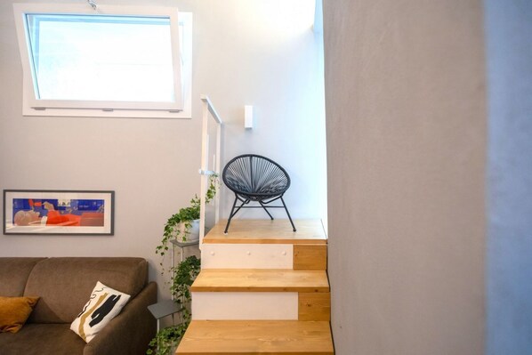 Una escalera con peldaños de madera, una silla negra, un cuadro enmarco y una ventana.