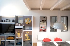 Un interior moderno con zona de comedor, una estantería con objetos decorativos y una lámpara colgante.