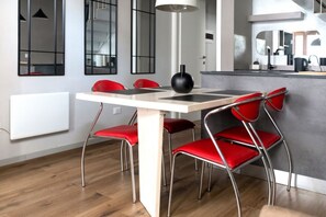 Una cocina moderna con una mesa blanca, sillas rojas y un florero negro.
