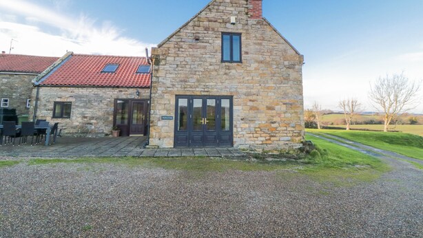 A stone building with a red-tiled roof, a black door, and a small window. - Wheelhouse Cottage (Whitby)