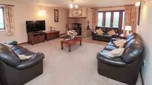 A living room with a fireplace, leather sofas, a coffee table, and a television. - Wheelhouse Cottage (Whitby)