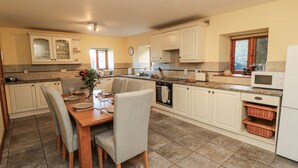 A spacious kitchen with white cabinets, a dining table set for four, and a microwave. - Wheelhouse Cottage (Whitby)