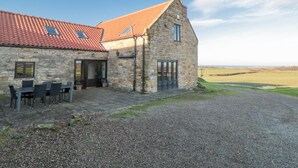 A stone building with a red-tiled roof, a gravel driveway, and outdoor seating. - Wheelhouse Cottage (Whitby)