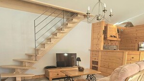 A living room with a wooden staircase, a television, a sofa, and a chandelier. - House in the heart of the Jura (Saint-Laurent-en-Grandvaux)