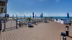Una terraza con sillones y sombrillas, con vista a una piscina y al océano.