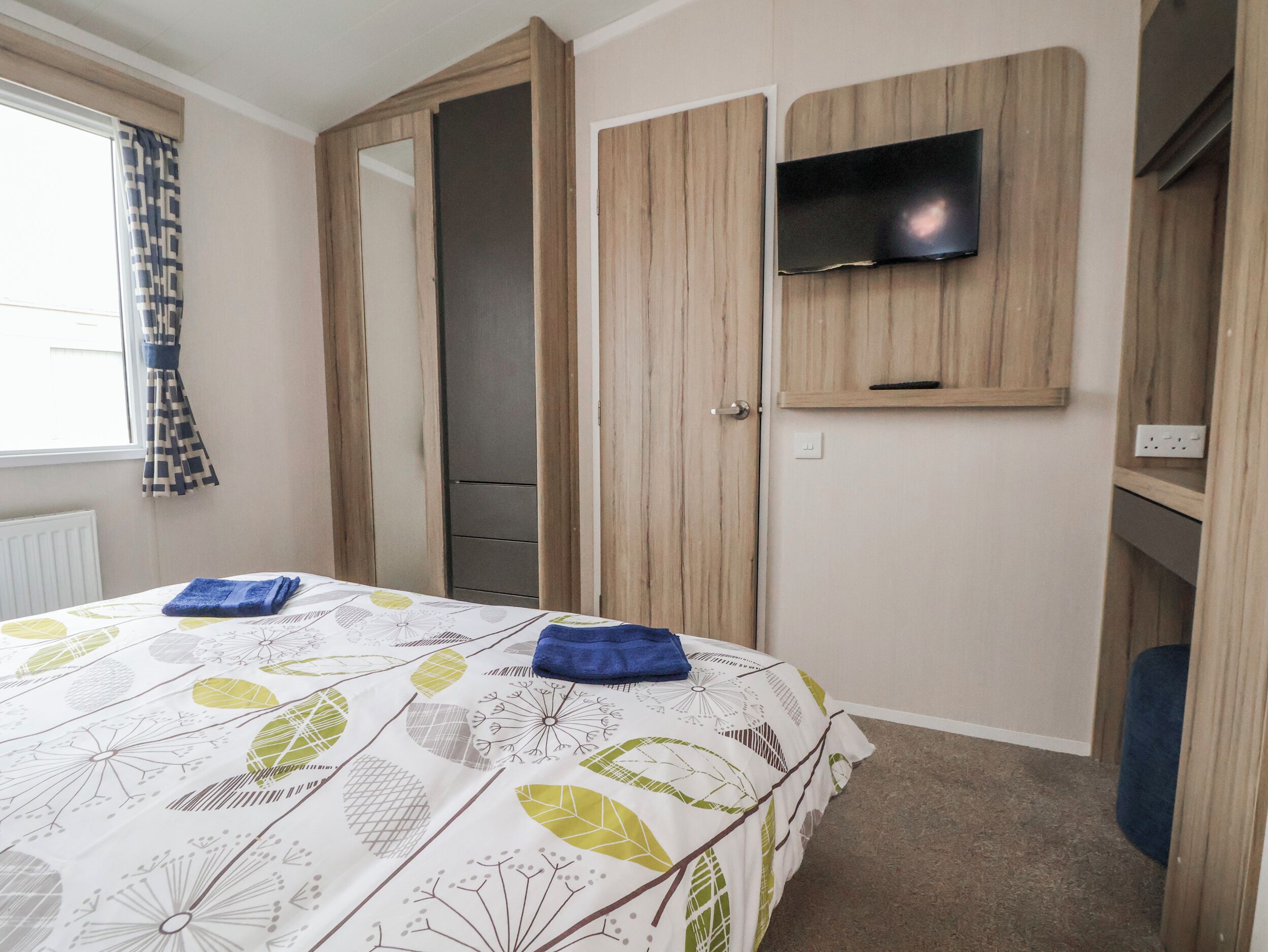 A bedroom with a bed, a wardrobe, a television, and a window with curtains.