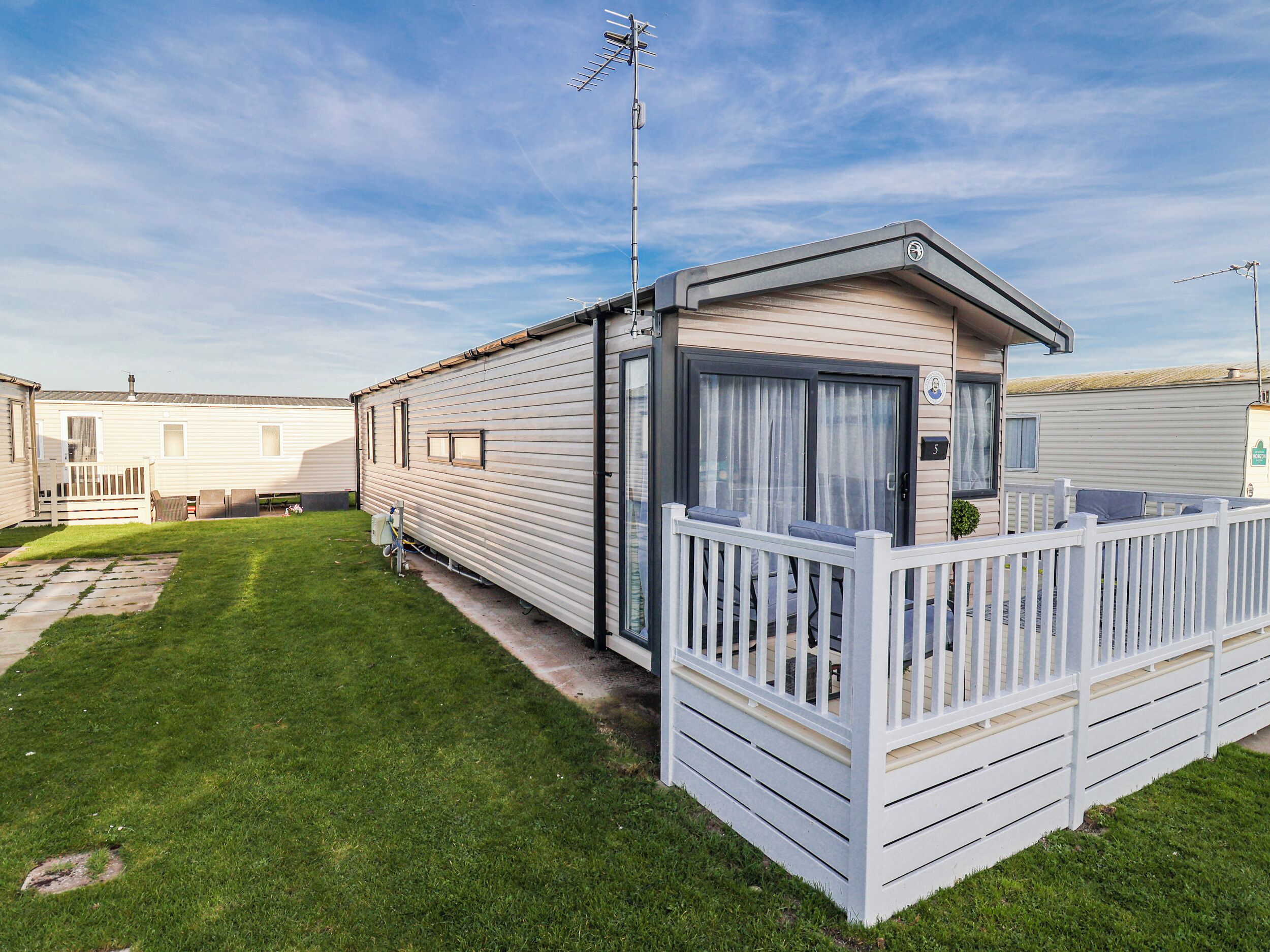 A mobile home with a fenced porch, a satellite dish, and a grassy yard.