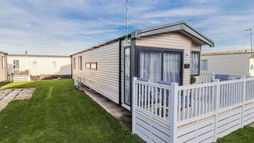 A mobile home with a fenced porch, a satellite dish, and a grassy yard.