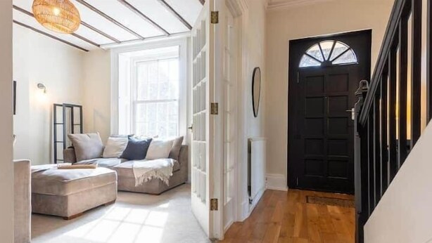 A cozy living room with a sofa and ottoman, a large window, and a black door. - Hall Gowen, Carnforth (Carnforth)