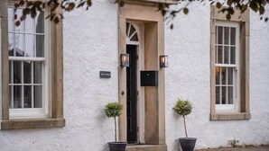 A white building with a central entrance, two potted plants, and two wall-mounted lights. - Hall Gowen, Carnforth (Carnforth)