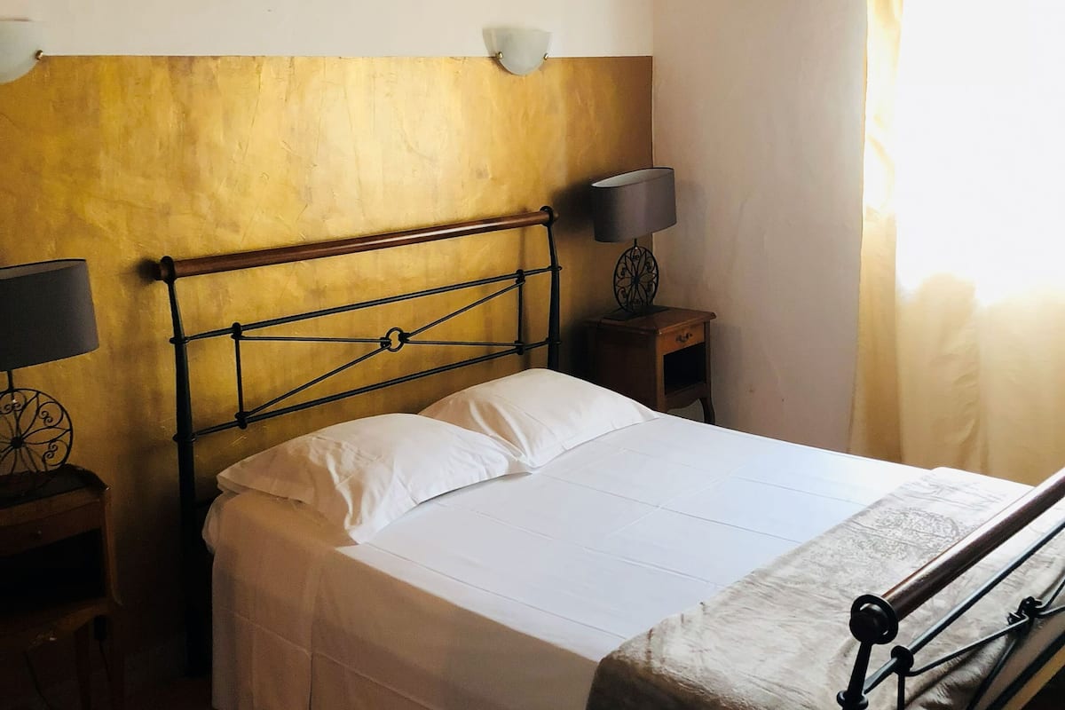 A single bed with a metal frame, a bedside table with a lamp, and a window with curtains.