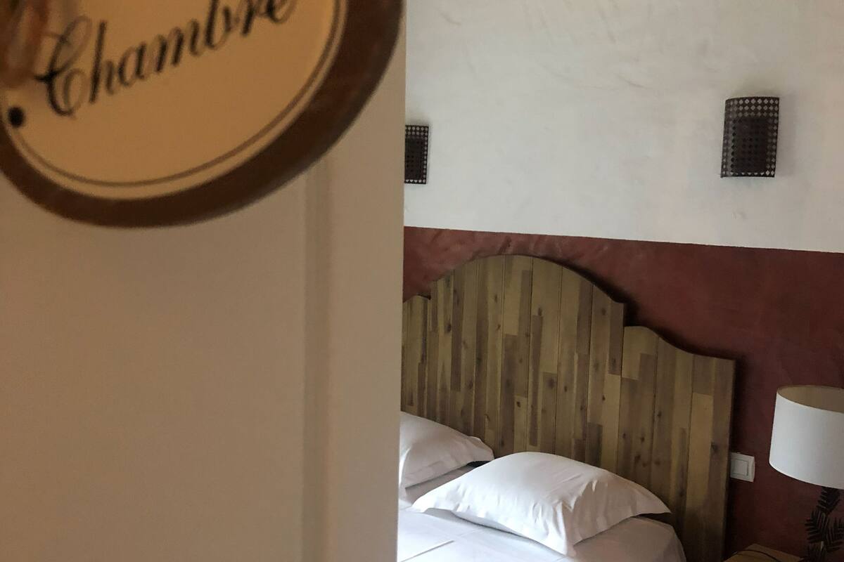 A bedroom with a wooden headboard, a bed with white linens, a nightstand with a lamp, and a wall-mounted light fixture.