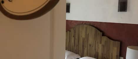 Un dormitorio con cabecera de madera, cama con ropa blanca, mesita de noche con lámpara y una lámpara de pared.