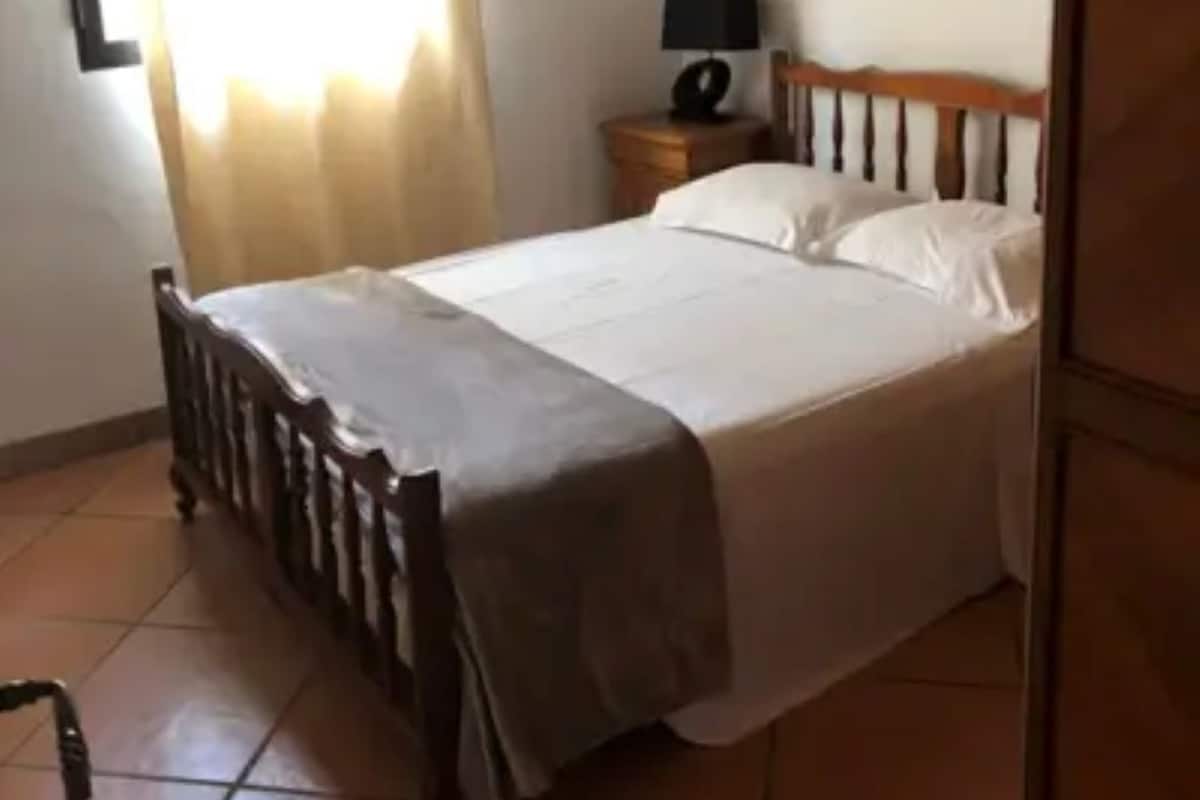 A bedroom with a bed, a nightstand, a lamp, and a window with curtains.
