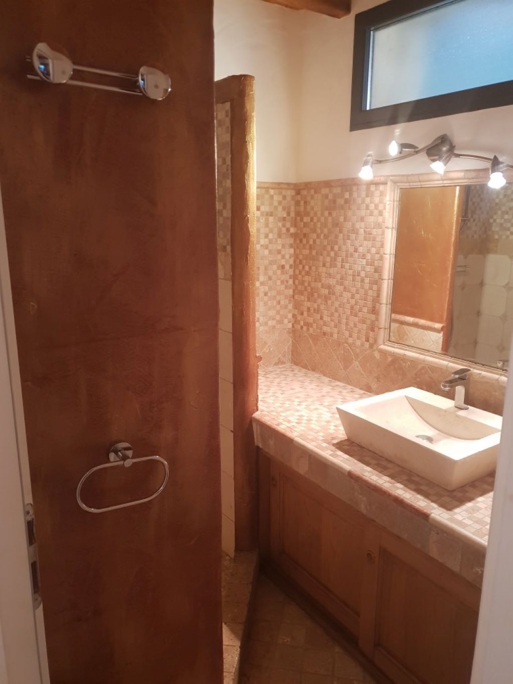 A bathroom with a wooden door, a tiled backsplash, a sink with a mirror, and a towel rack.