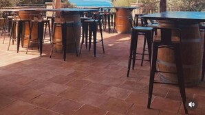 An outdoor patio with wooden tables and chairs, a rustic wooden ceiling, and a view of the sea. - Domaine Santu Matteu (Olmeto)