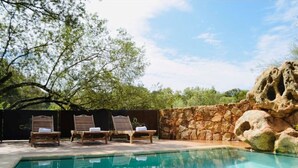 A pool area with lounge chairs, a stone wall, and trees in the background. - Domaine Santu Matteu (Olmeto)