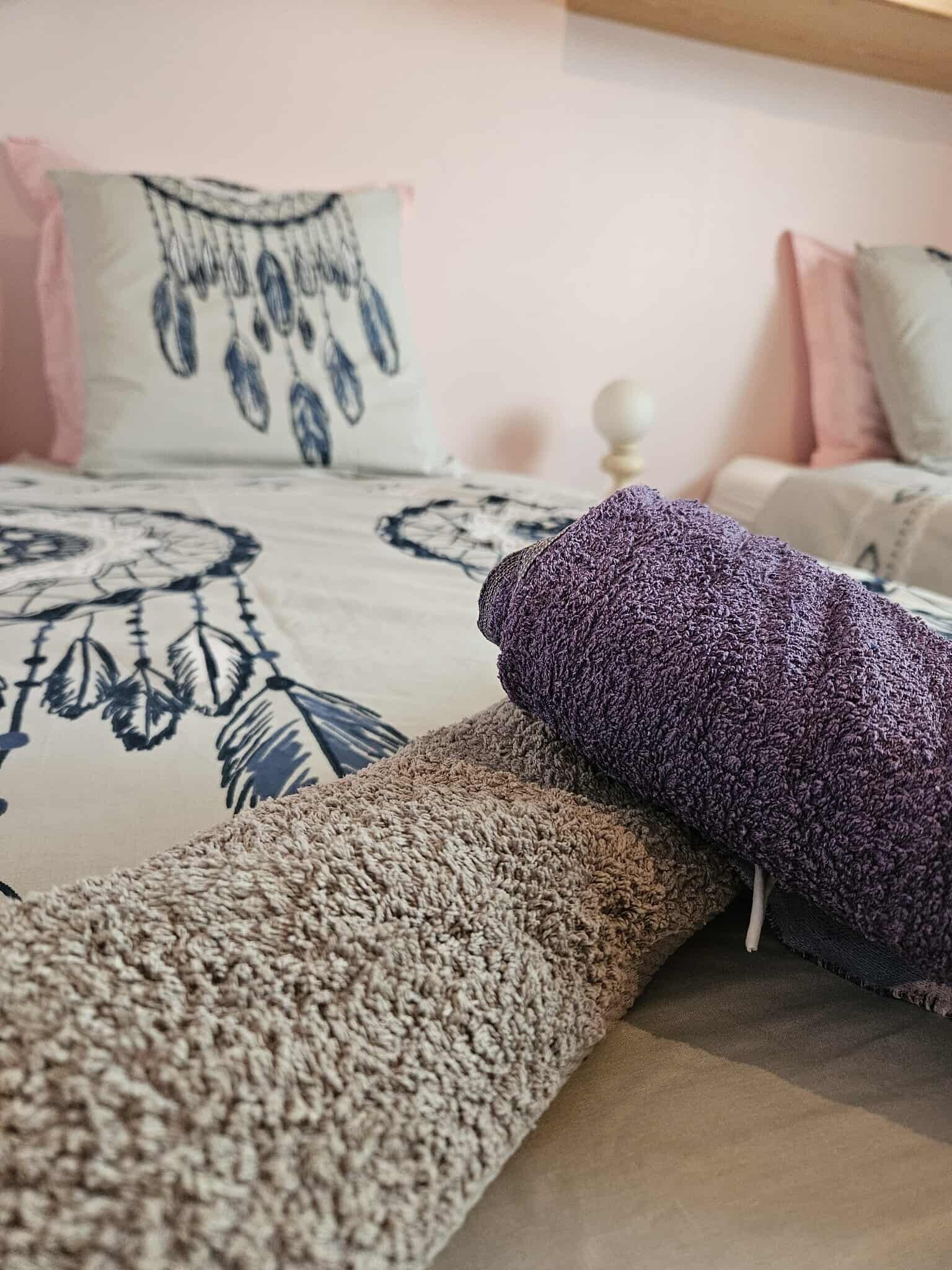 Una cama con una colcha estampada, un cojín decorativo y una manta enrollada.