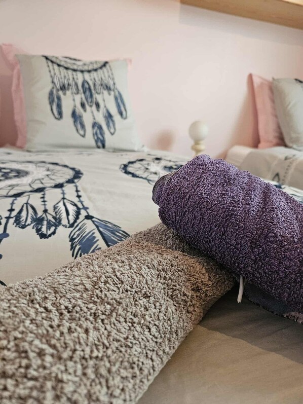 A bed with a patterned bedspread, a decorative pillow, and a rolled-up blanket.
