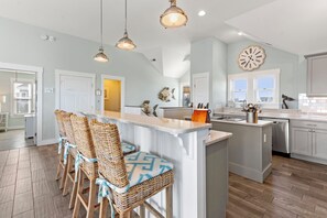 A kitchen with a central island, bar stools, pendant lighting, a clock, and a view of the outside. - Saltwater Pool | Hot Tub | Elevator | Rec Room (Salvo)
