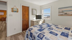 Een slaapkamer met een bed, een bureau, een televisie, een raam met uitzicht en een plafondventilator.