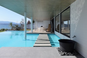 A modern pool area with a clear view of the sea, a stone pathway leading to the pool, and a large black water feature.