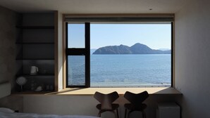 A bedroom with a large window, a bed, two chairs, a small table, and a white cabinet.