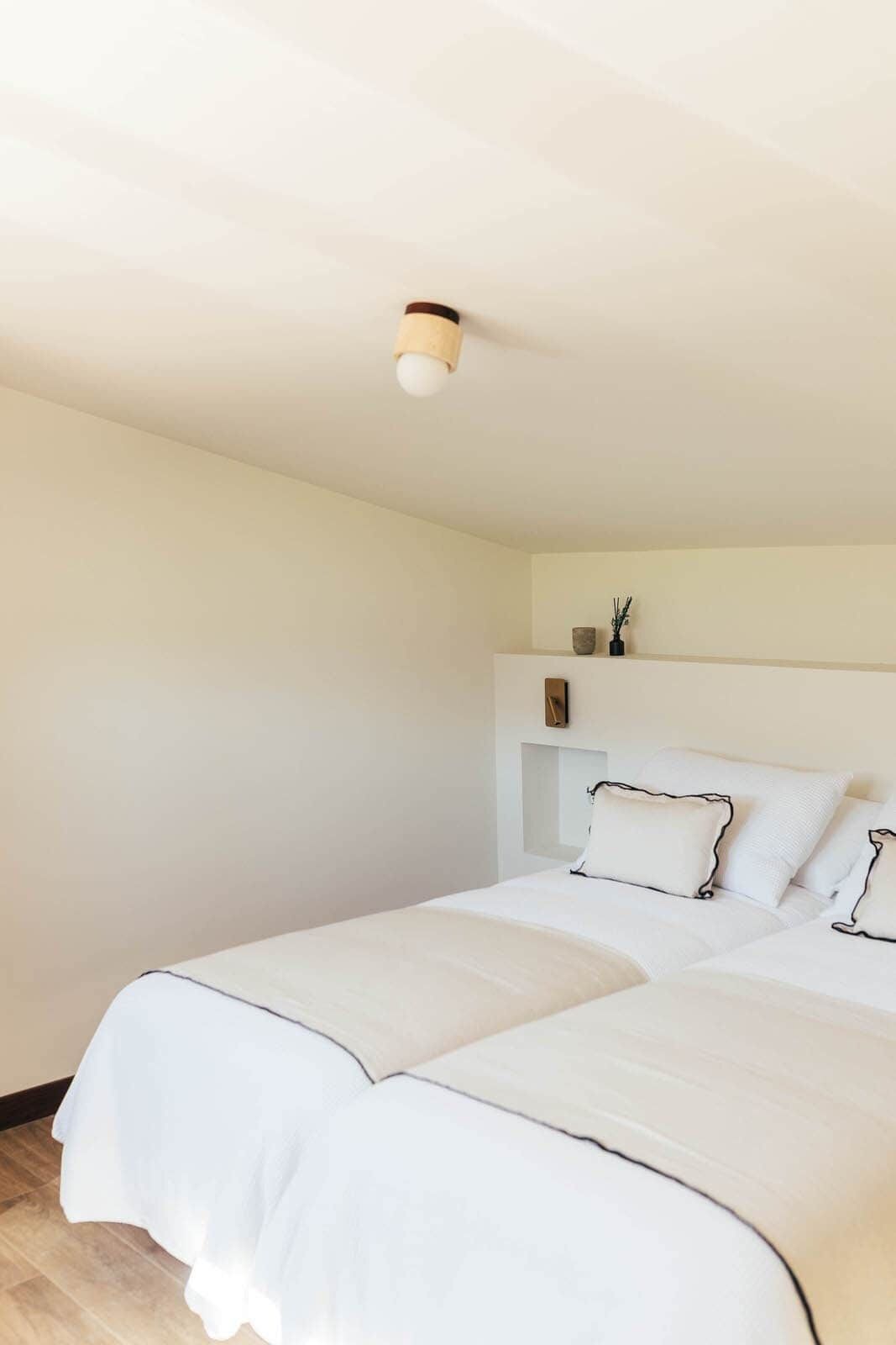 Une chambre à coucher comprenant un lit, une table de chevet, une étagère murale décorative et un luminaire au plafond.