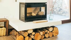 Ein moderner Kamin mit Holzscheiten, einem weißen Sims und einer klaren Glasscheibe.