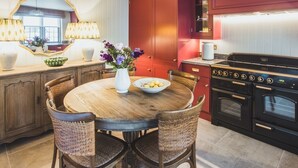 Una cocina con una mesa redonda de madera, sillas de mimbre, un espejo grande y un horno doble.