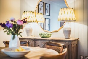 A dining area with a wooden table, two chairs, a vase with flowers, and two lamps on a cabinet.
