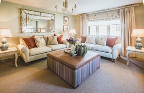 A living room with a sofa, ottoman, and two side tables with lamps. - Luxurious Cotswolds Apartment in Chipping Campden (Chipping Campden)