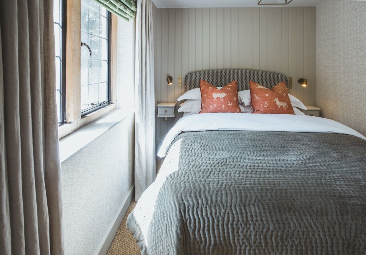 Una habitación de hotel con una cama, cortinas, una mesita de noche y un ventanal.