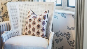 Una habitación con una silla de mimbre blanca, un cojín estampado y papel tapiz floral.