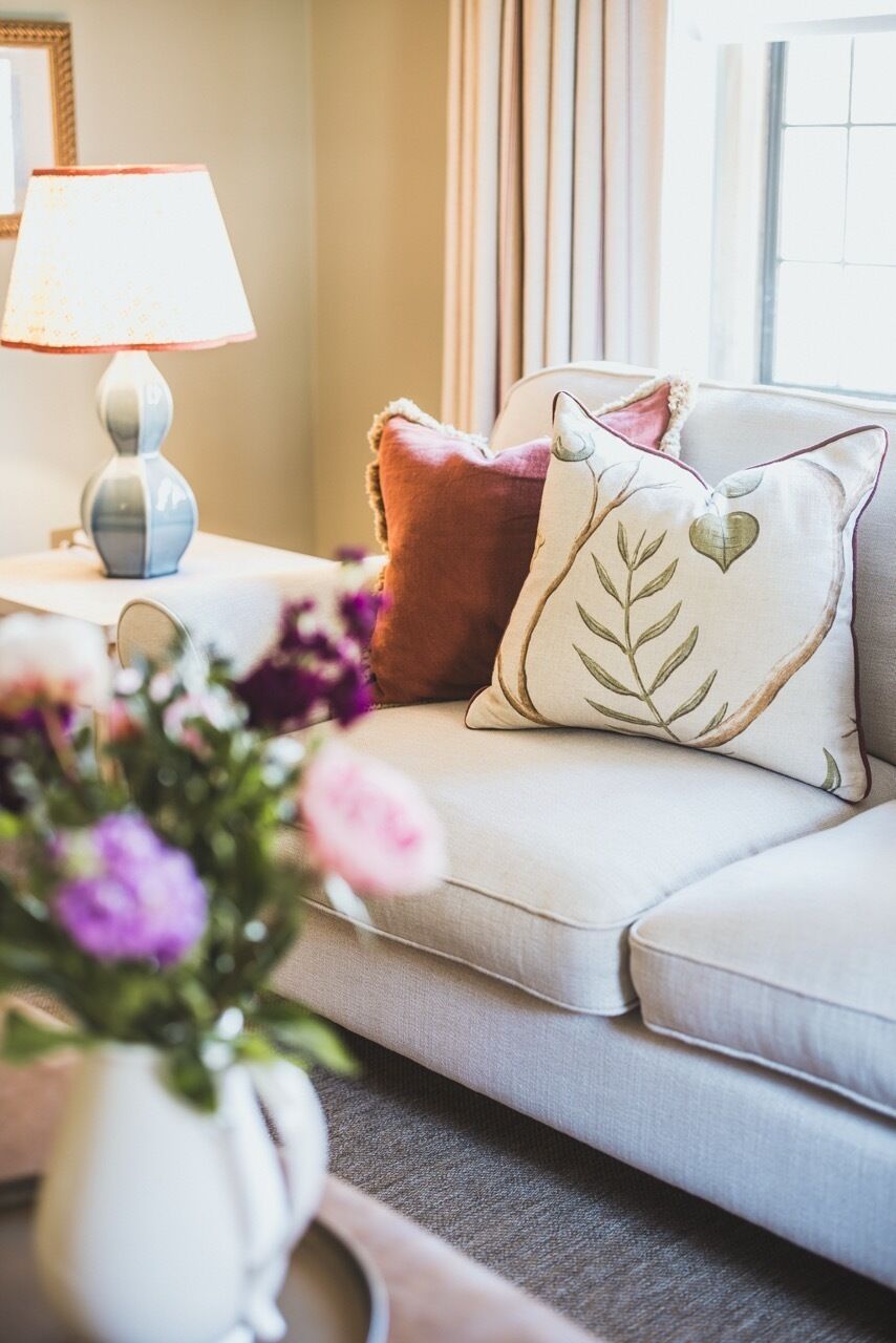 A well-lit room with a sofa, a lamp, and a vase with flowers.