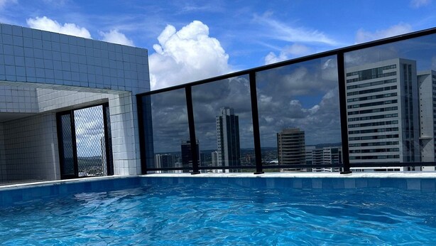 Piscina com água azul cristalina, cercada por edifícios modernos e um céu límpido.