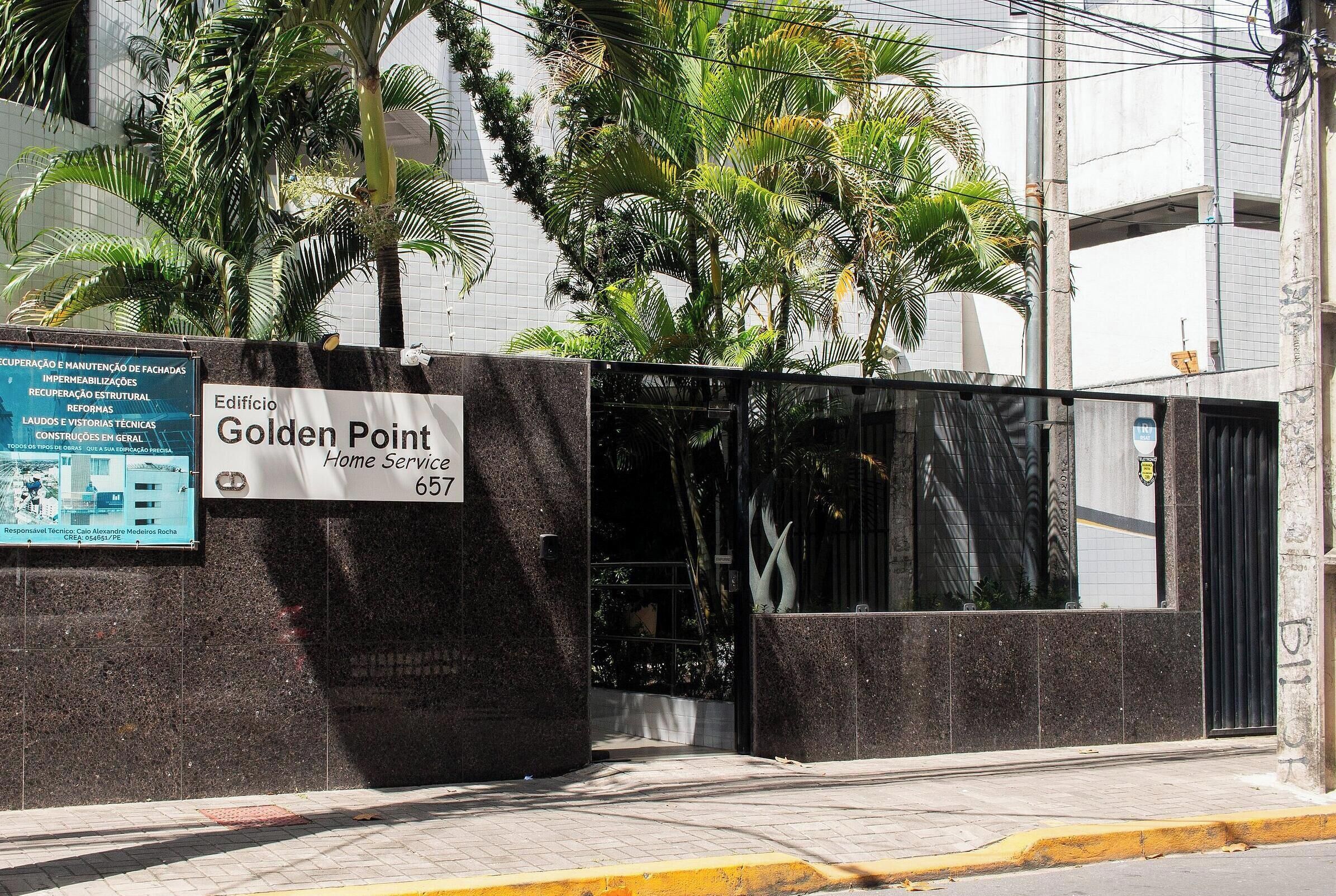 Une entrée sécurisée, fermée par un portail, mène au bâtiment de Golden Point Home Service. Une plaque indique l’adresse et les services proposés.