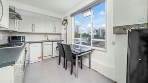 Cozinha compacta com armários brancos, fogão preto, pia e janela com vista para a cidade.